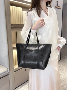 Chic black oil wax leather tote bag with shoulder straps shown in an elegant interior setting