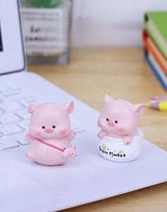 Cute pink resin pig figurines displayed on a wooden desk with a laptop and books
