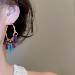 Close-up of model wearing gold hoop earrings with vibrant colorful petal pendants