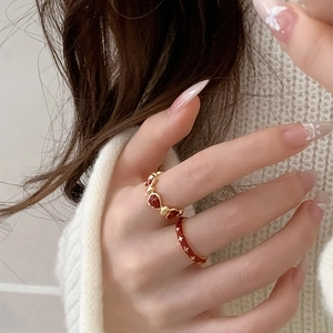 Detail of red heart flower rings on hand with golden accents and enamel finish