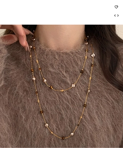 Détail du collier long plaqué or 18k avec œil de tigre et perle sur un pull marron