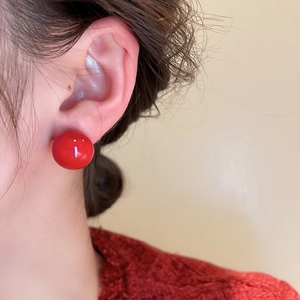 Close-up of minimalist red spherical stud earrings with a polished finish on model