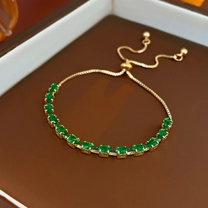 Close-up of golden adjustable snake chain bracelet with green oval gemstone in a box