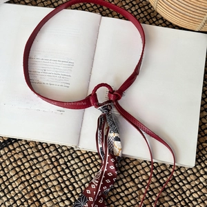 Detail of a red leather cord belt with a vintage patterned silk scarf knot on a book