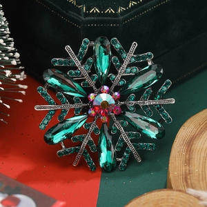 Macro shot of silver snowflake brooch with green teardrop crystals and festive pine background