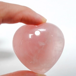 Primer plano de un colgante de cuarzo rosa natural con forma de corazón y acabado liso