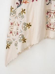 Detail of bohemian embroidery and scalloped lace edge on a cream linen dress