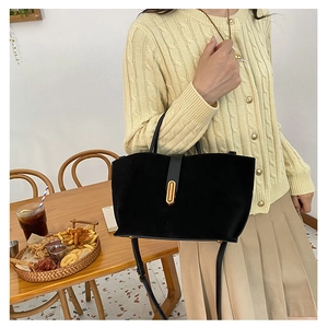 Detail of black suede tote bag with golden oval buckle and elegant shoulder strap design