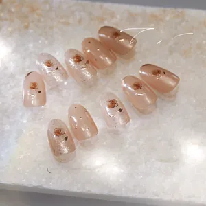 Macro view of peach pink press-on nails with golden rose patterns and glitter details