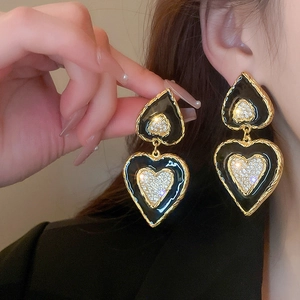 Close-up of vintage gold earrings with black heart enamel and sparkling crystals on model