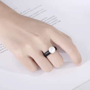 Detail of minimalist wide black ceramic ring with center pearl worn on hand