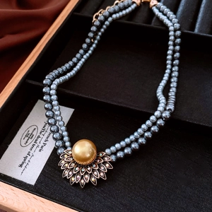 Détail du collier de perles grises à double rangée avec perle dorée et base florale sertie
