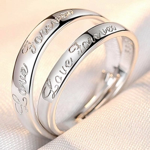 Close-up of silver couple rings engraved with Love Forever on soft white fabric