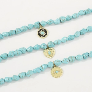 Detail of three turquoise stone necklaces with sun, heart, and evil eye gold pendants