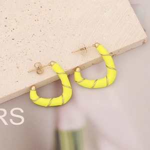 Detailed shot of yellow enamel earrings with golden metal wire on a stone background