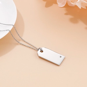 Close-up of a silver polished rectangular pendant with a small diamond on a beige surface