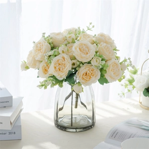Gros plan de roses artificielles crème et verdure en vase de verre pour déco