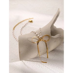Elegant 18k gold plated bow necklace with white pearls draped on a ceramic vase