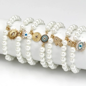 Detail of beaded bracelets featuring golden Evil Eye and Hamsa Hand charms on white display