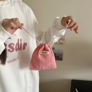 Pink pleated drawstring storage bag with woven label being opened by hand