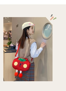Detail of red plush tomato-shaped crossbody bag with cute facial features and green stem