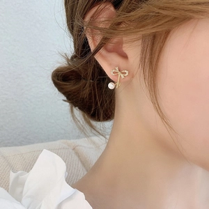Detail of elegant gold bow earrings with sparkling stones and a hanging pearl on ear