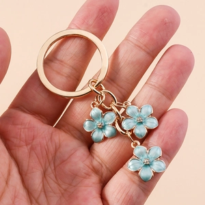 Sweet light blue cherry blossom keychain with gold finish held in hand, floral accessory
