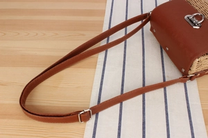 Detail showing woven paper straw texture and brown leather strap with silver metal buckle