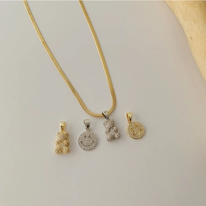 Macro detail of gold snake chain with micro-pave zircon bear and smiley face pendants