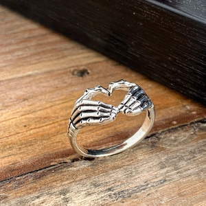 Detailed view of Gothic skeleton hand heart ring with vintage silver finish on wood