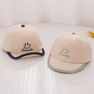 Détail de casquettes bébé beiges avec broderie Smile et bords roulés contrastés