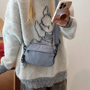 Blue-grey nylon crossbody phone bag shown on shoulder with minimalist style