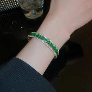 Macro detail of gold-plated open bracelet with emerald crystals and zircon accents