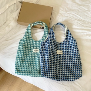 Blue and white checkered knit tote bag showing spacious design on a bed setting