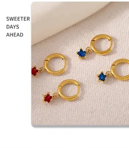 Close-up of gold 18K plated star earrings with red and blue glass stones on white knit