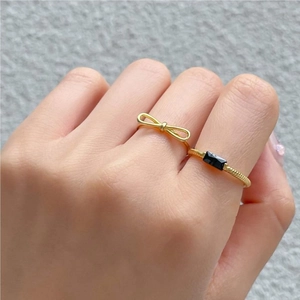 Detail of gold bow ring and minimalist black rectangular gemstone band on fingers