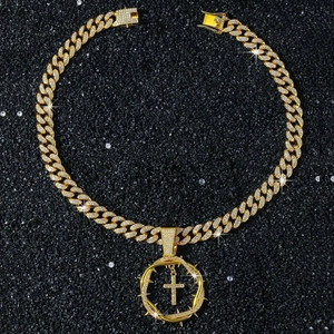 Detailed view of iced-out gold Cuban chain with thorn-wrapped cross pendant on black surface