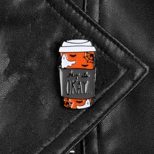 Detail of coffee cup enamel pin with Halloween motifs on black leather jacket surface