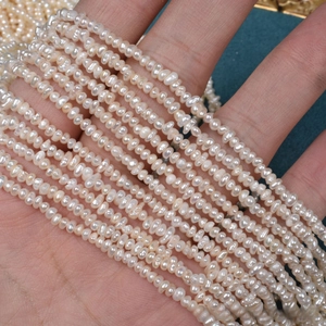 Macro view of 2.5mm natural freshwater mini flat pearls held in hand for size contrast
