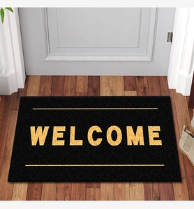 Detail of black welcome doormat with gold lettering and coconut husk texture on wood floor