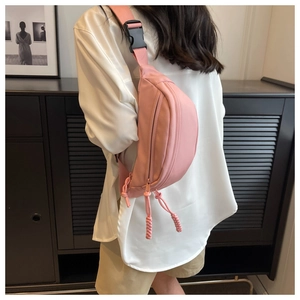 Rear view of a model wearing a soft pink canvas chest bag with adjustable black buckle strap