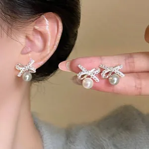 Macro detail of 18K silver bow earrings with sparkling cubic zirconia and white pearls