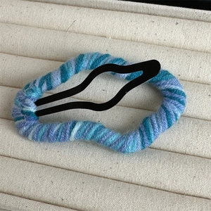Macro detail of cloud-shaped wool wrapped BB hair clip on a beige display tray