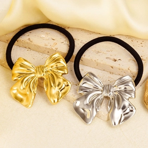 Detail of gold and silver bow hair ties on a stone block with soft silk fabric background