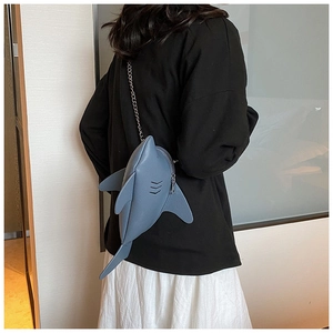 Blue shark crossbody bag with silver chain strap shown on a model's white skirt outfit