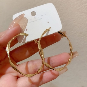 Close-up of luxury gold hammered twist hoop earrings worn to show size and texture