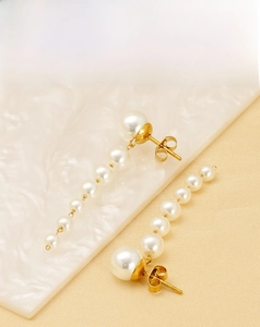 Close-up of elegant gold tassel earrings with seven graduated white pearls on marble
