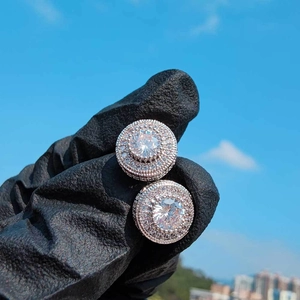 Macro detail of round zircon hip hop stud earrings held against a bright blue sky background