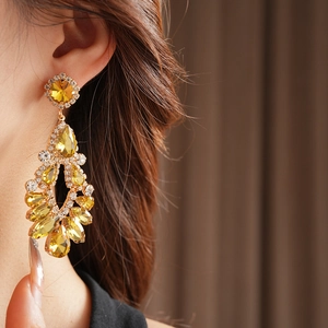 Detail of a large gold-plated teardrop earring with yellow crystals on a female model