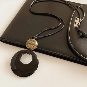 Dettaglio del ciondolo ad anello in agata nera con perla a righe su un portafoglio nero